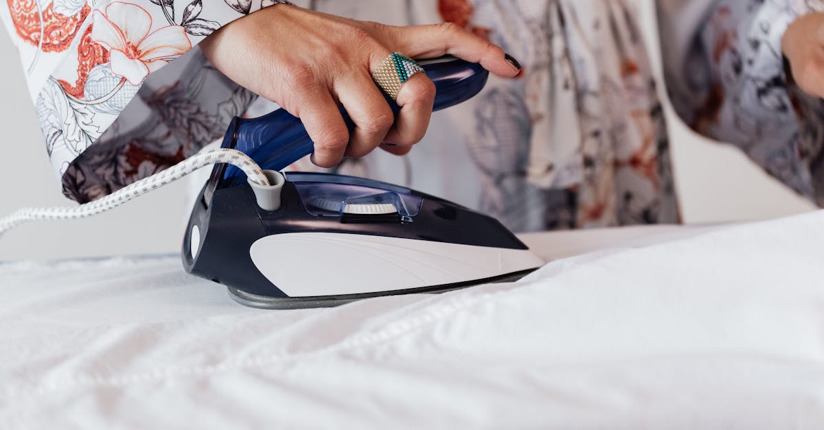 crop anonymous housewife wearing elegant silk robe and stylish ring ironing white clothes with moder